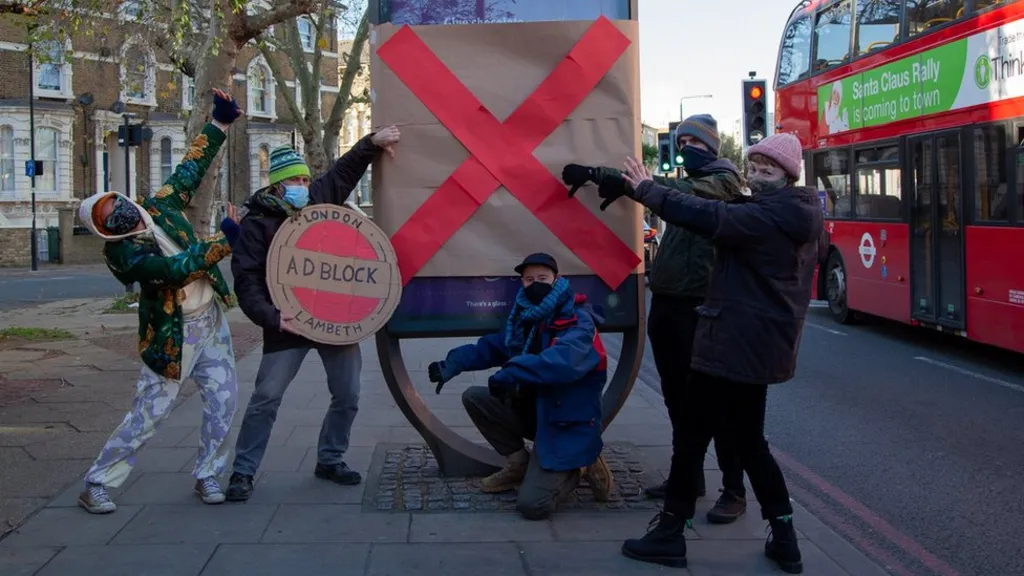 People in London standing near an ad that's been taped over with a big red 'X'